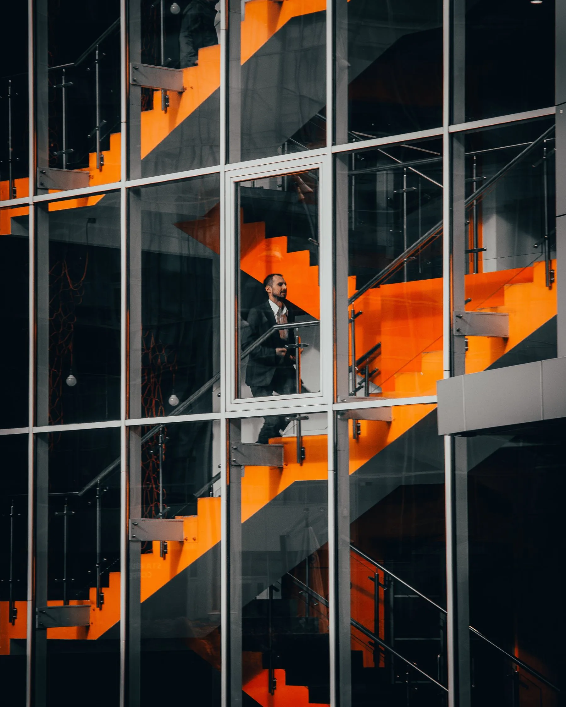 Businessman in a suit ascending a bold orange staircase in a modern glass office building
